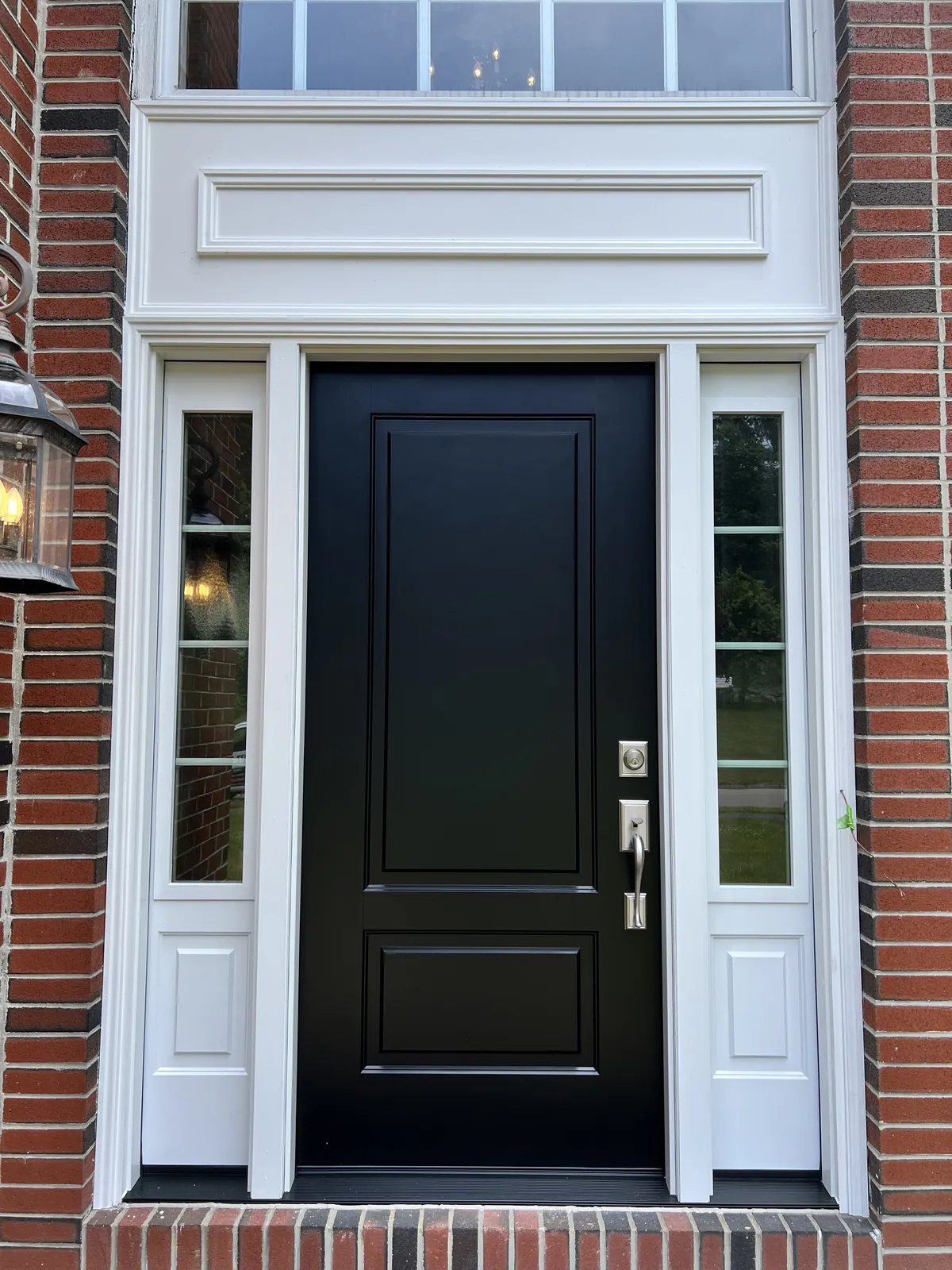 Black entry door with transom set into a brick facade
